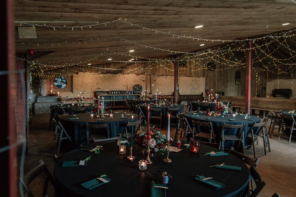interior of Comrie Croft one of the best Scottish barn wedding venues in scotland decorated for a reception with fairy lights and black tablecloths and jewel coloured flowers