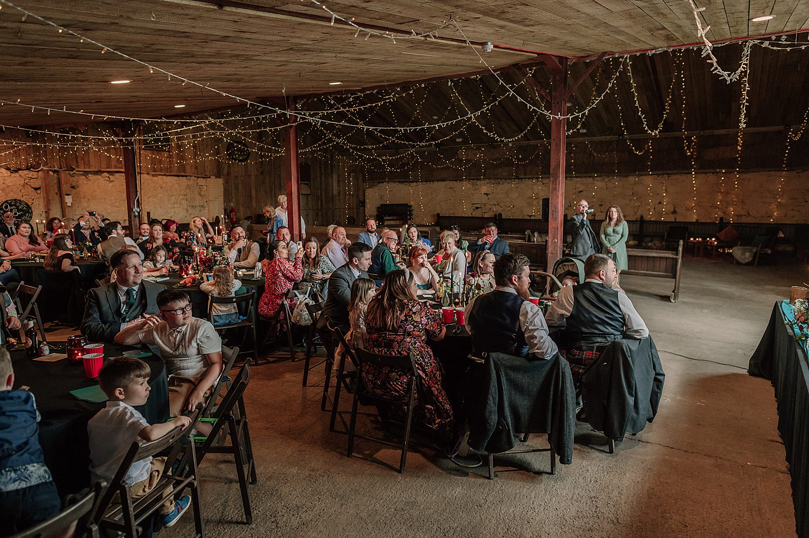 reception inside barn for a Comrie Croft wedding decorated with lots of fairy lights and black tablecloths