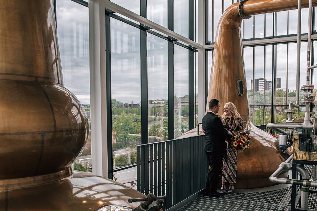 bride and groom standing beside pot still during their distillery wedding scotland at clydeside distillery