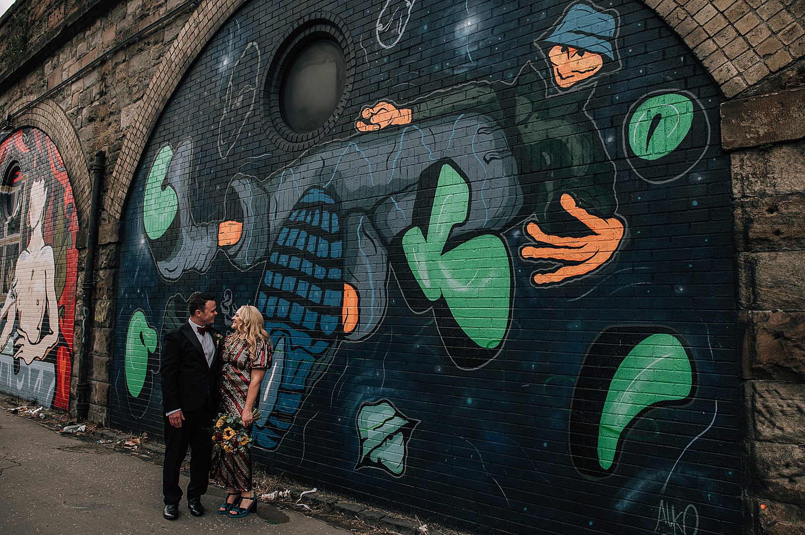 bride and groom standing in front of large mural at swg3 glasgow after their Scottish distillery wedding at clydeside distillery