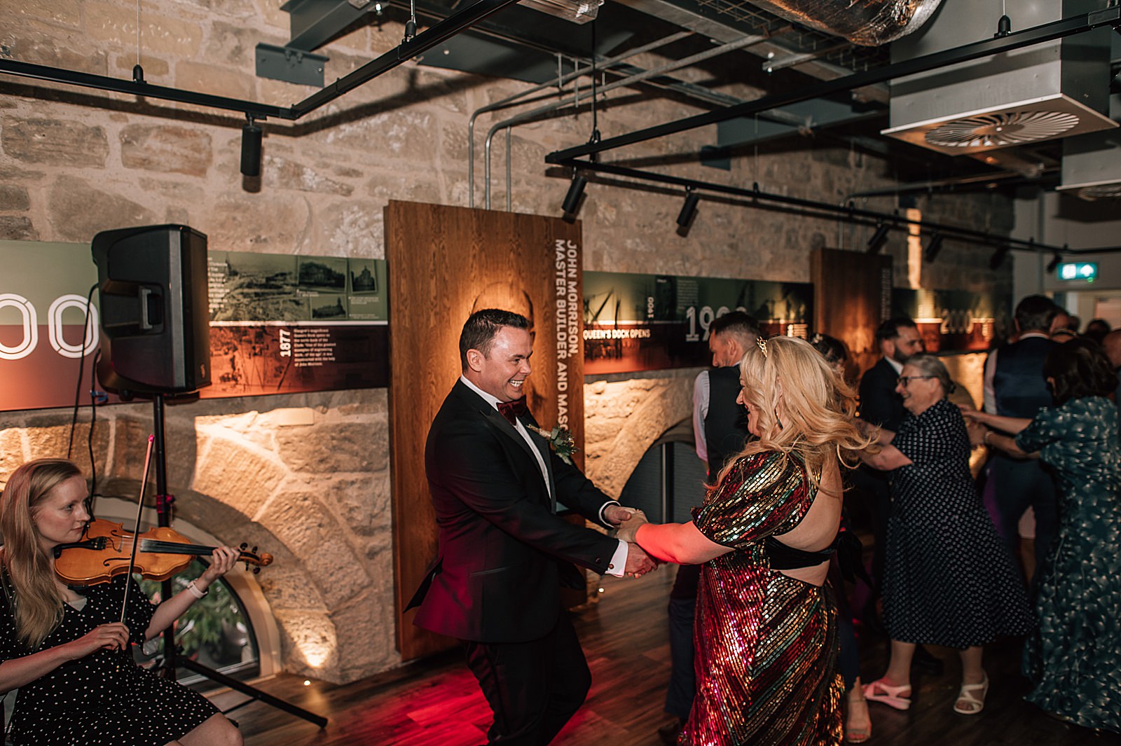 bride and groom ceilidh dancing at their distillery wedding scotland in clydeside distillery at night with ceilidh band
