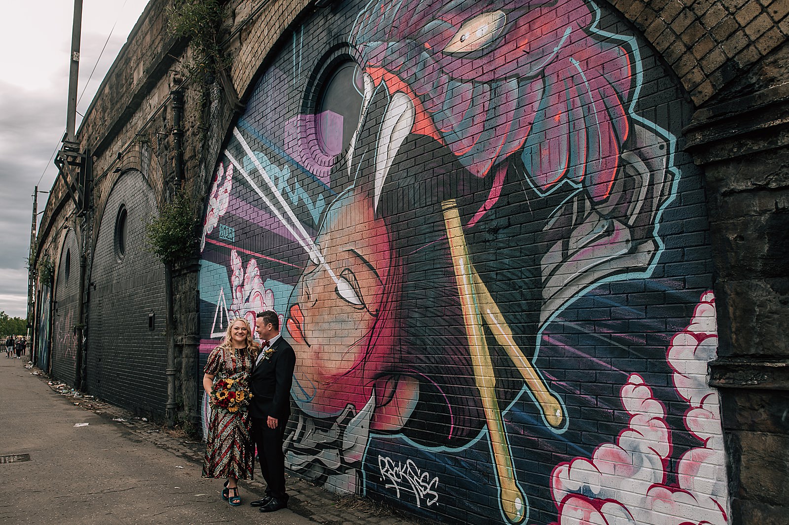 bride and groom standing in front of mural at SWG3 glasgow for wedding photos by alternative Scottish wedding photographer