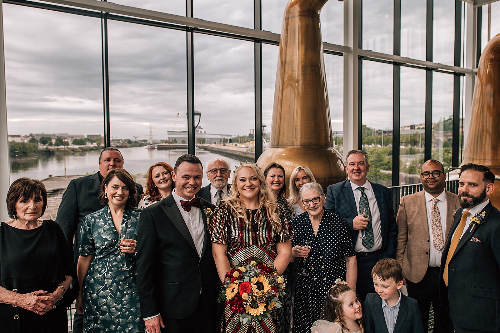 bride and groom with their family at their distillery wedding scotland at clydeside distillery in front of pot stills