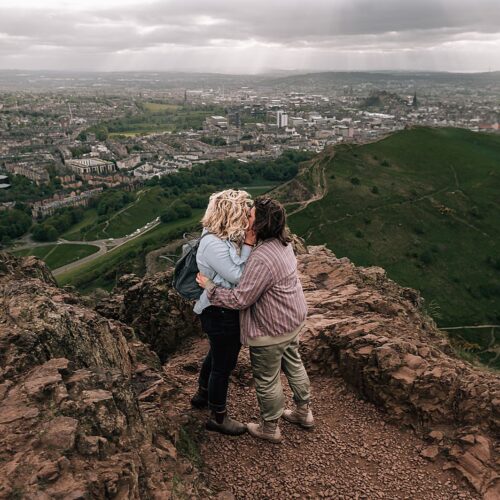 couple kissing standing on top of Arthurs seat during surprise proposal photo shoot captured by Edinburgh proposal photographer