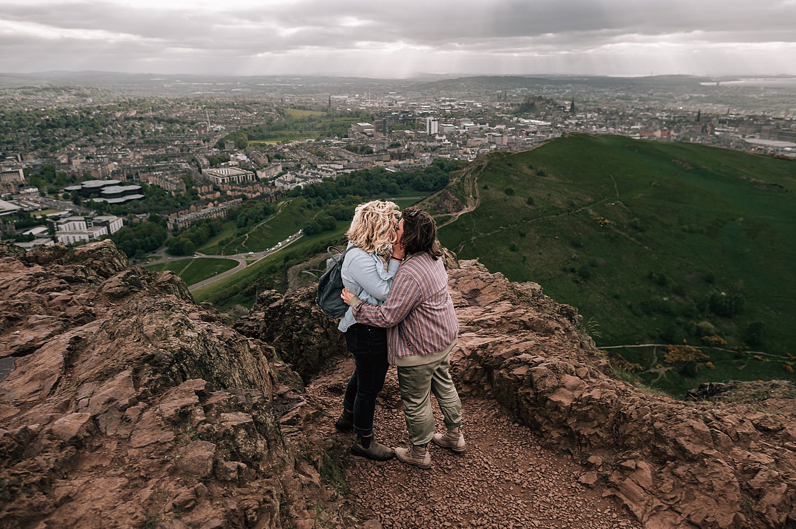 couple kissing standing on top of Arthurs seat during surprise proposal photo shoot captured by Edinburgh proposal photographer