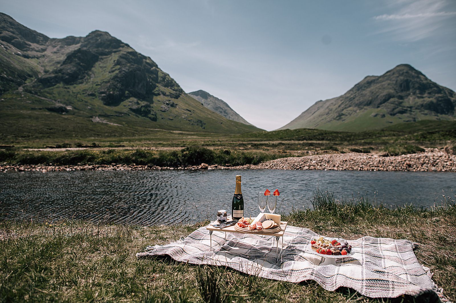 luxury Scottish picnic by the side of a burn in glencoe with champagne, cheese and strawberries captured by glencoe proposal photographer