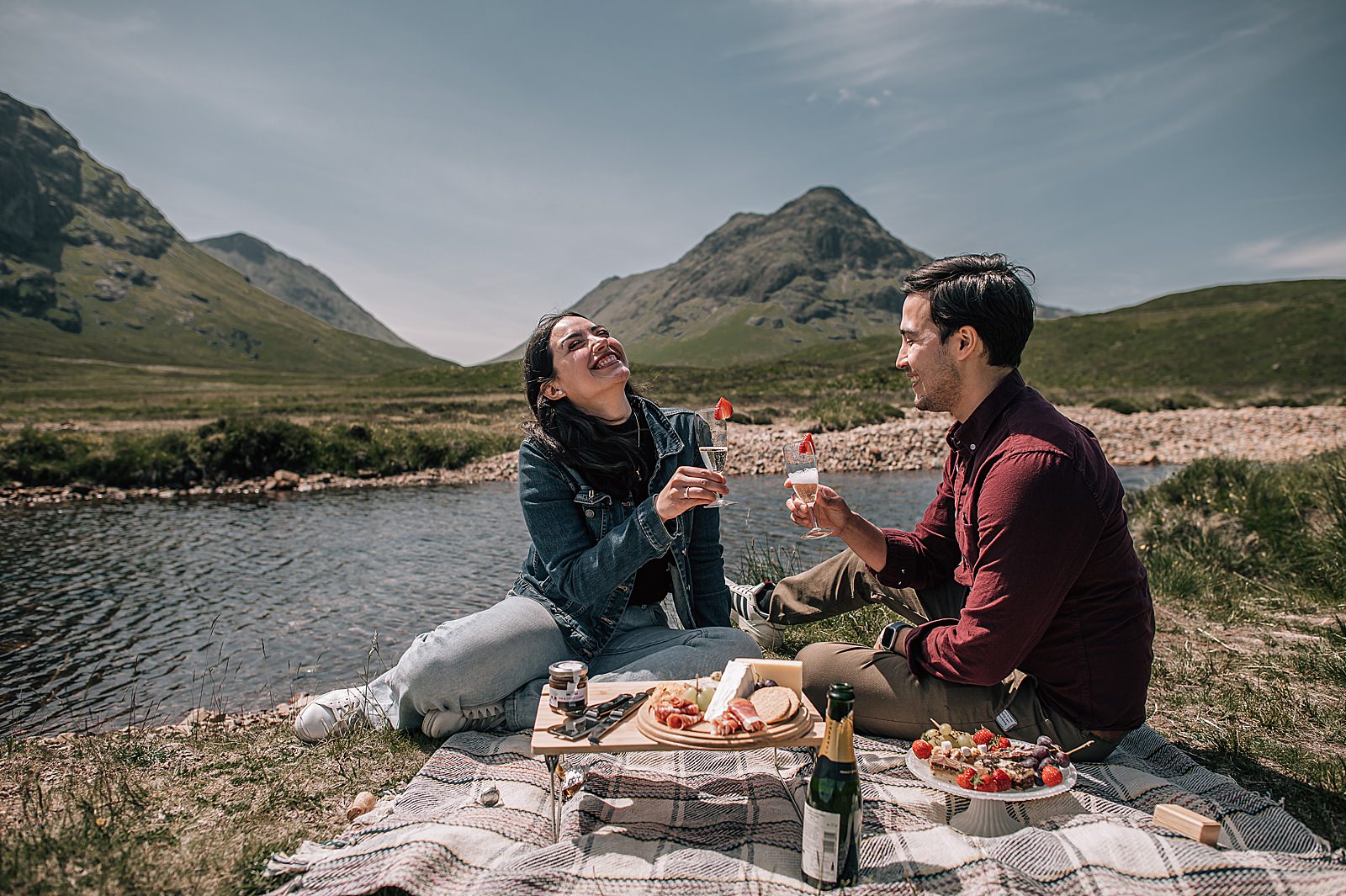 couple sitting on picnic blanket in glencoe with Scottish luxury picnic after surprise engagement captured by glencoe proposal photographer