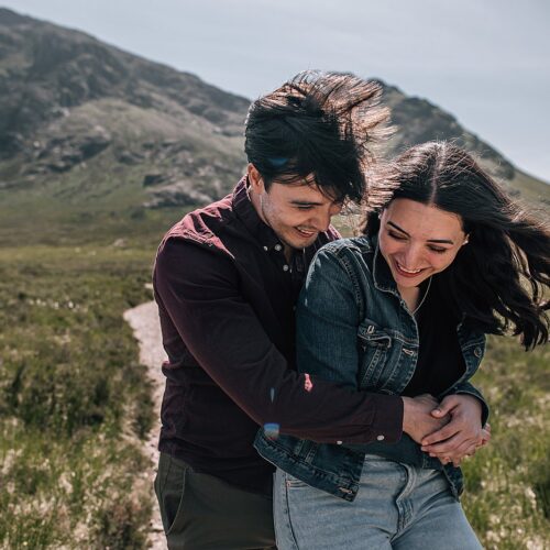 couple hugging and laughing in front of glencoe mountains for their glencoe proposal photographer shoot