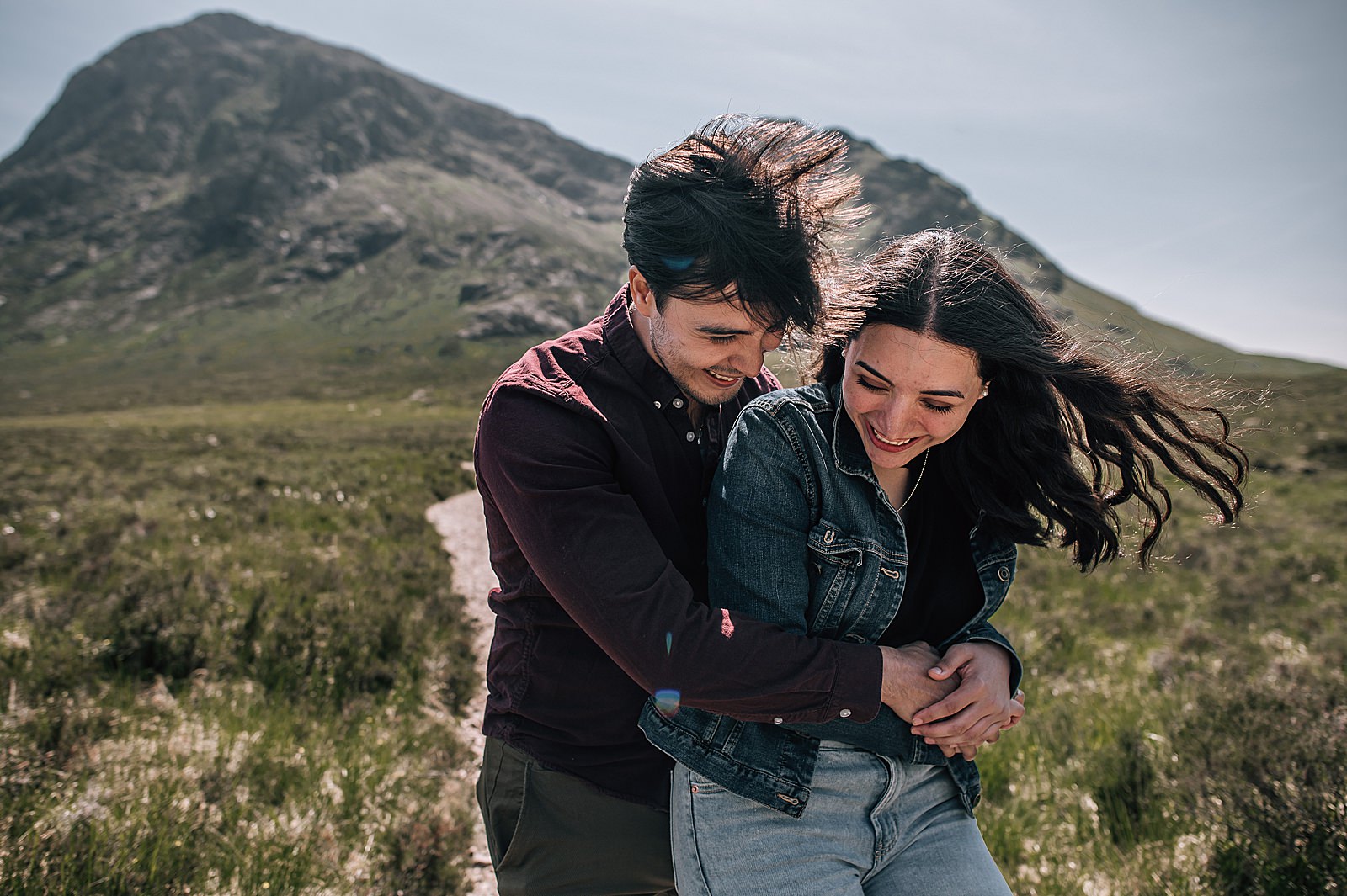 couple hugging and laughing in front of glencoe mountains for their glencoe proposal photographer shoot