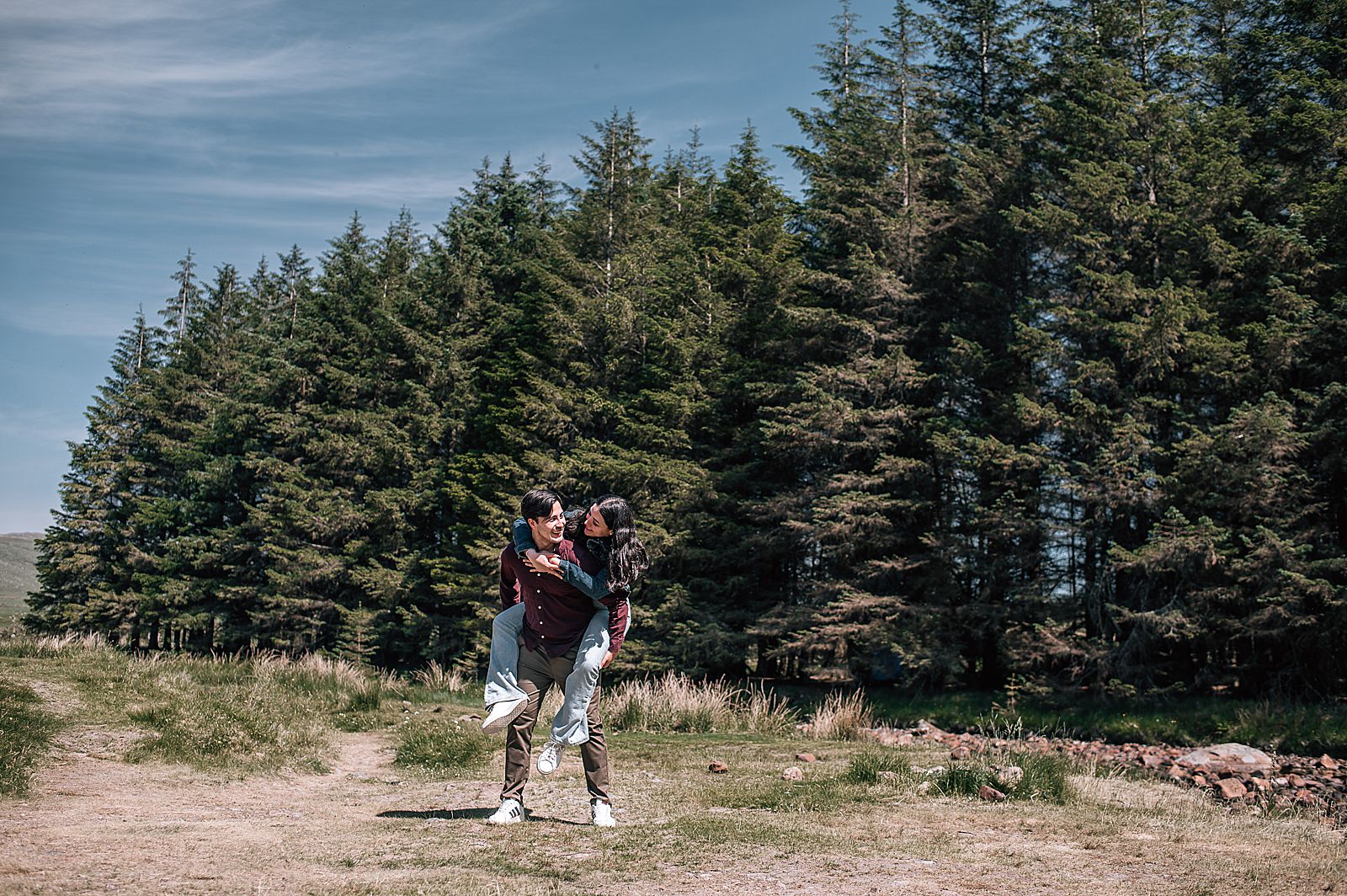 Scottish surprise engagement couple being playful and laughing in front of glencoe forest captured by glencoe proposal photographer