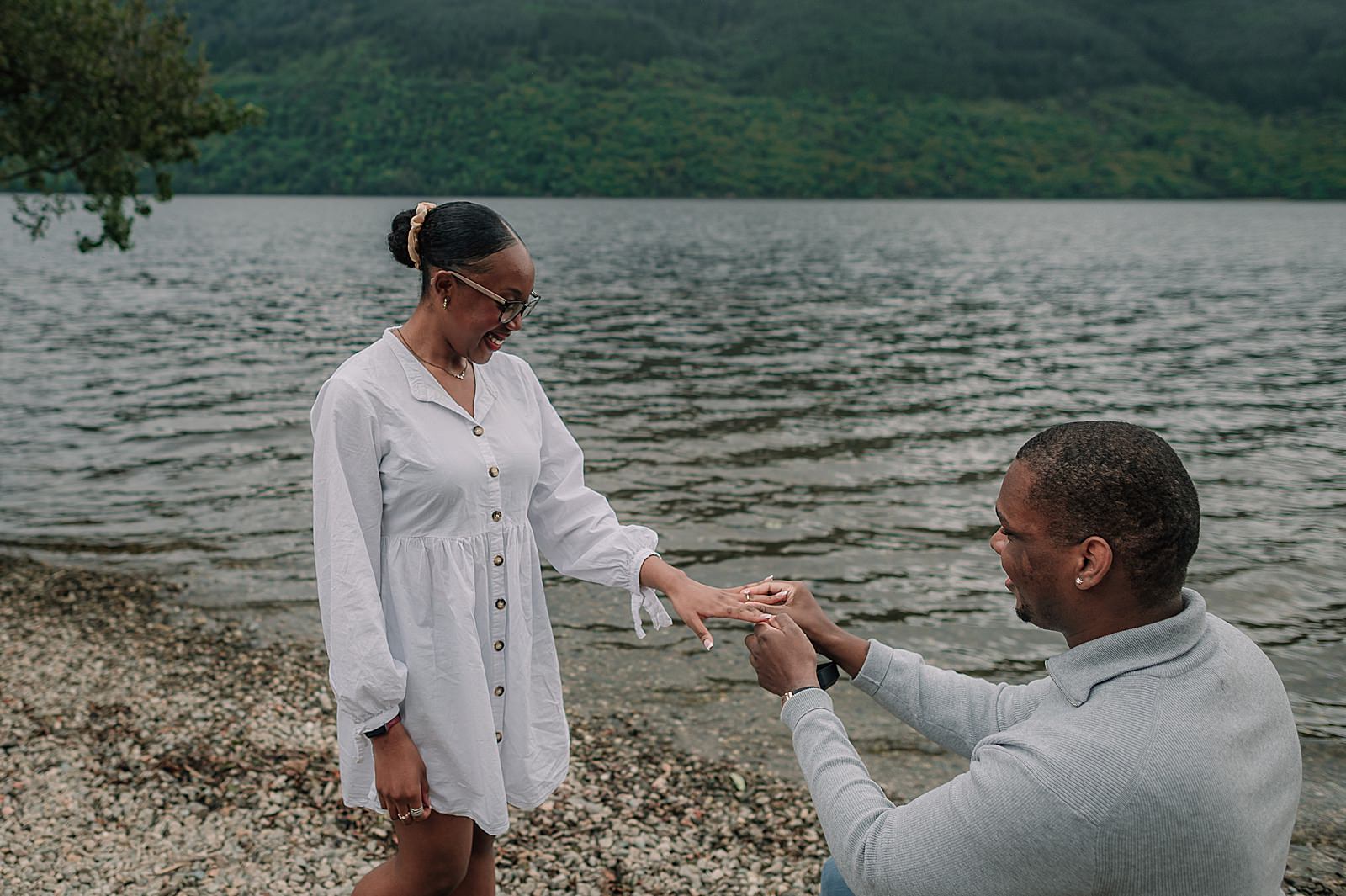 couple getting engaged with oval engagement ring on the shore at Loch Lomond at firkin point captured by proposal photographer scotland