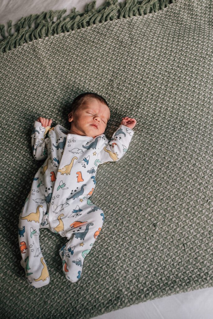 sleeping newborn baby in dinosaur sleepsuit