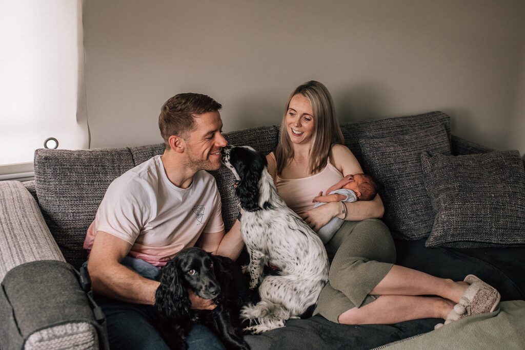 man with spaniels sitting on sofa next to wife with newborn baby