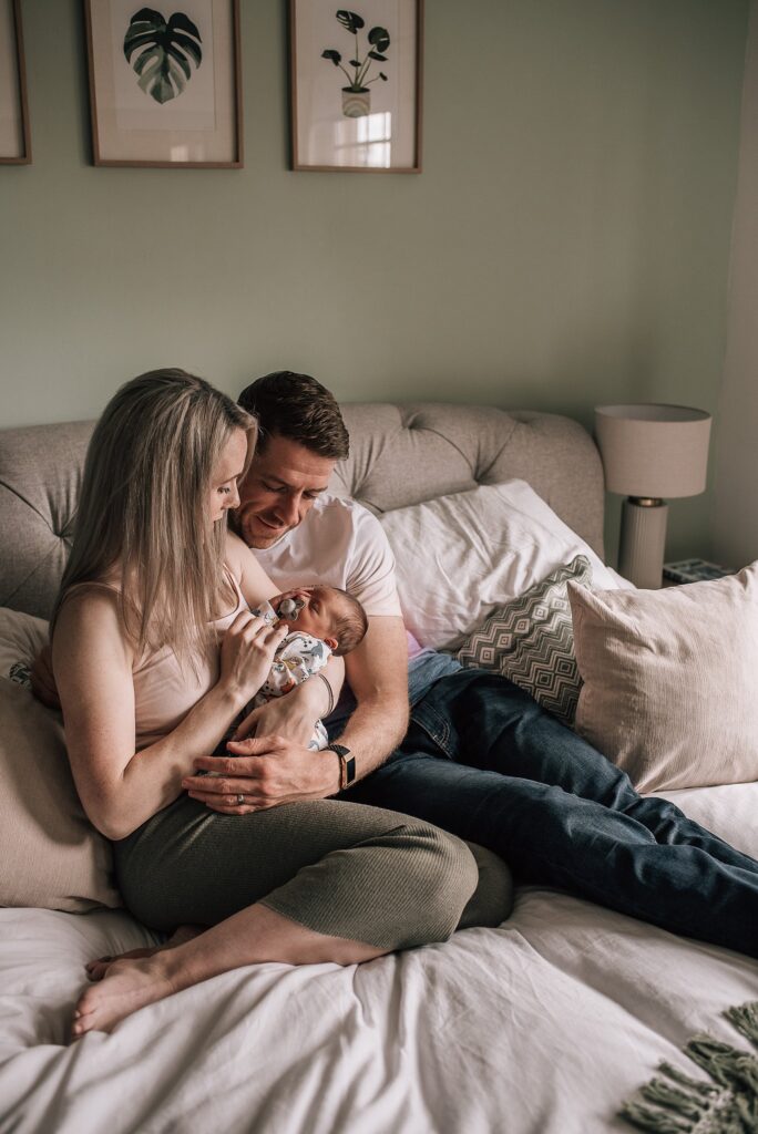 parents cuddling newborn baby on a bed