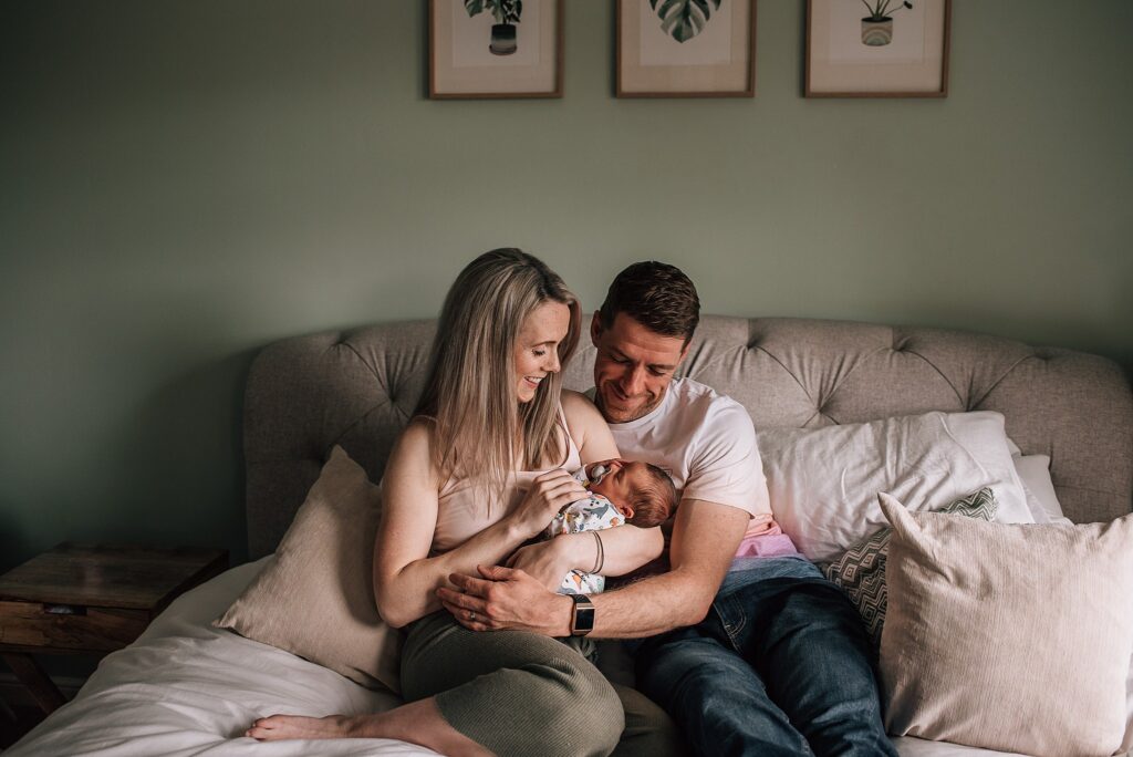 couple sitting on a bed cuddling their newborn baby