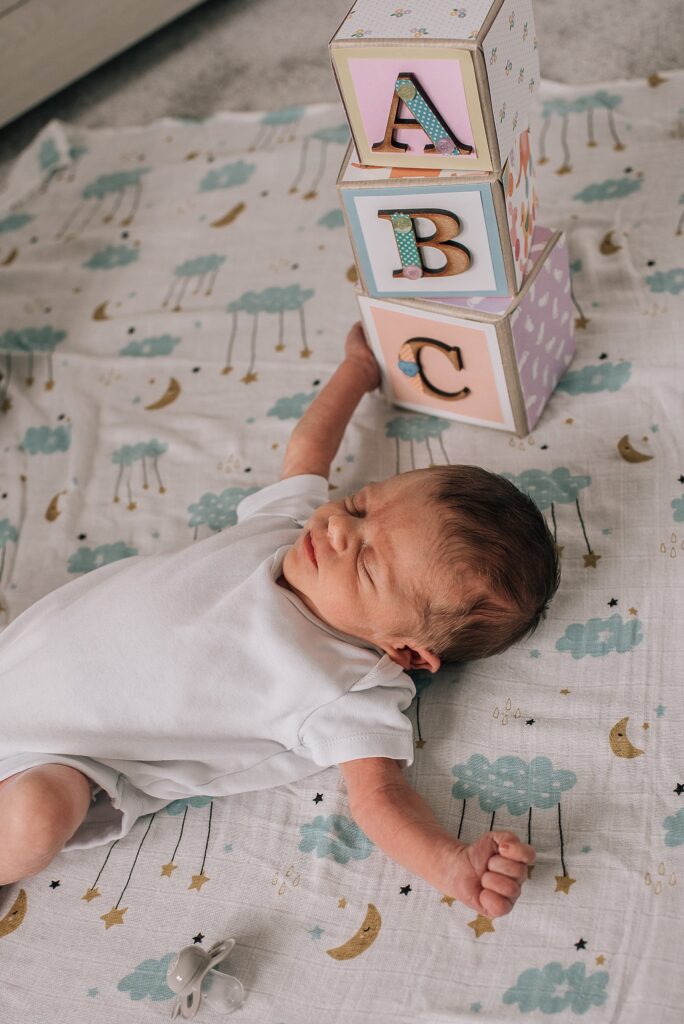 baby lying on patterned blanket next to building blocks