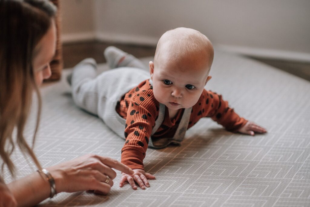 baby lying on tummy looking towards mother's hand