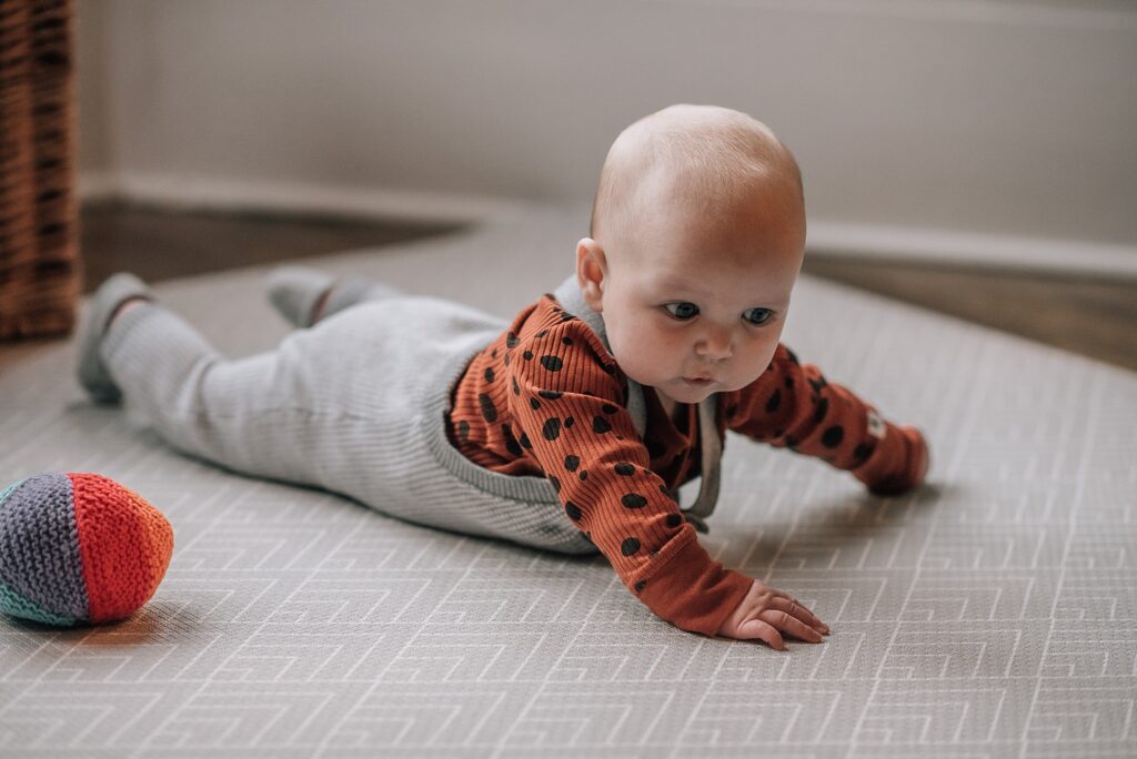 baby lying on her tummy raising her head next to a knitted ball