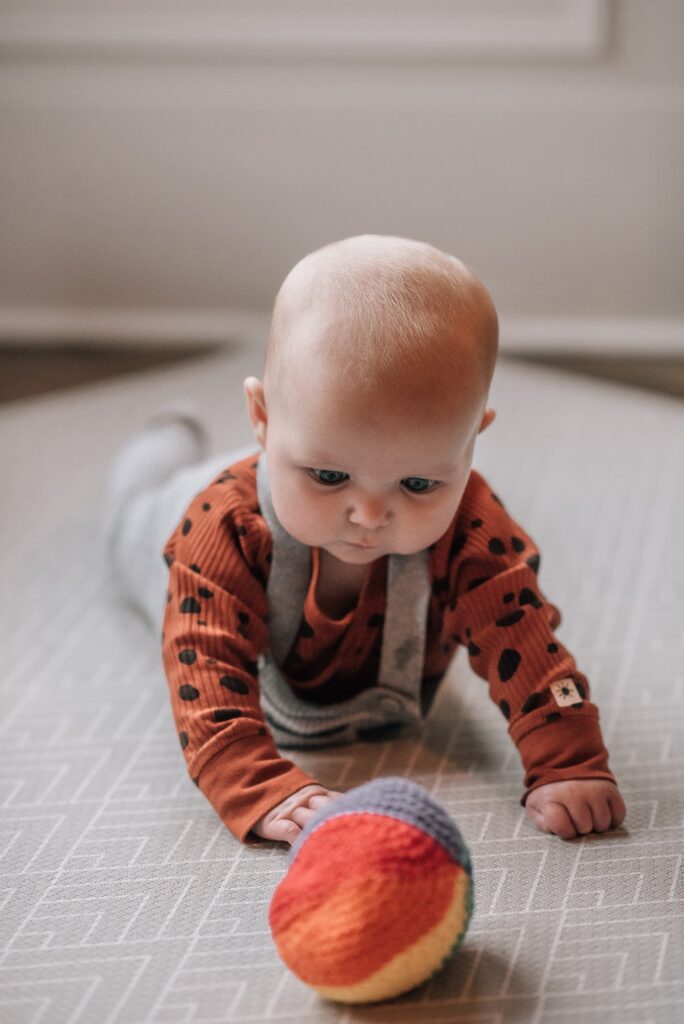 baby lying on her tummy, lifting her head looking at a toy ball