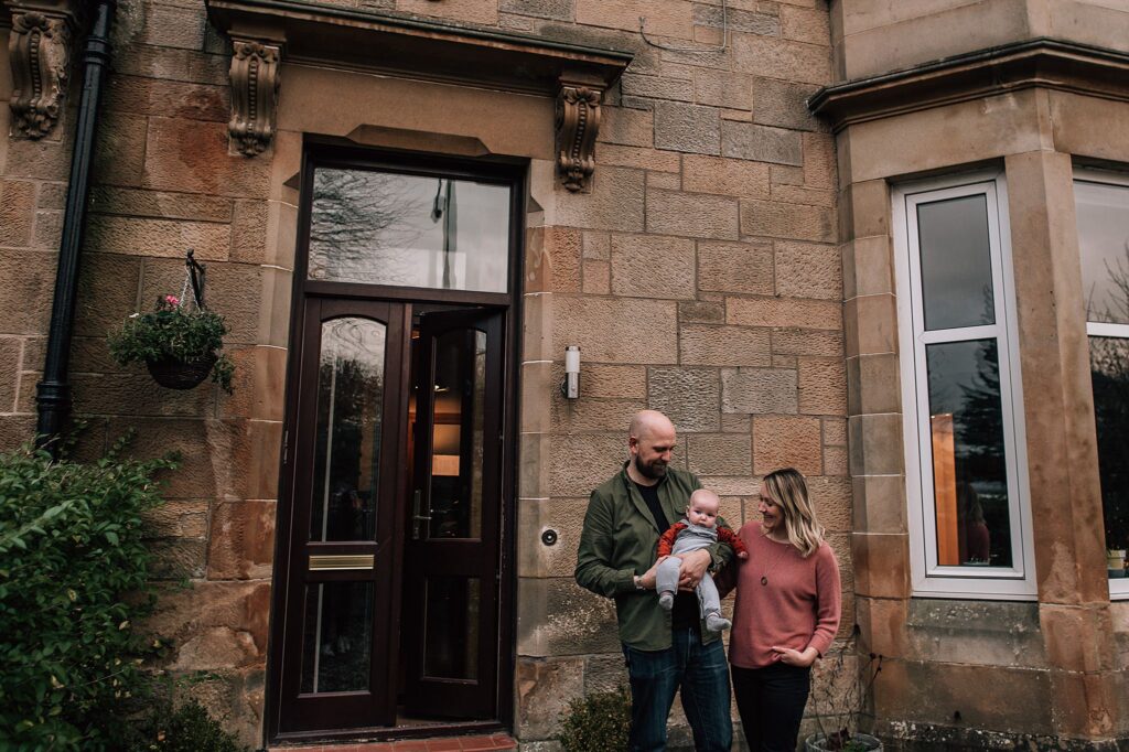 young couple standing outside Glasgow victorian sandstone home with their baby
