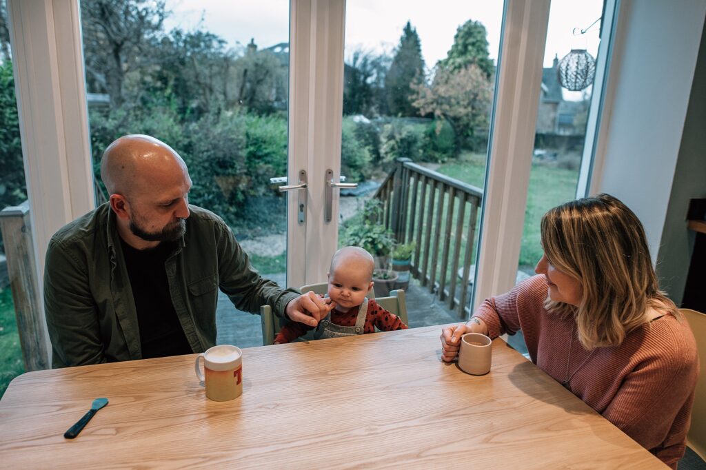 parents sitting at a wooden table with their baby