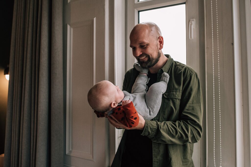 man with a green shirt and beard playing with a baby