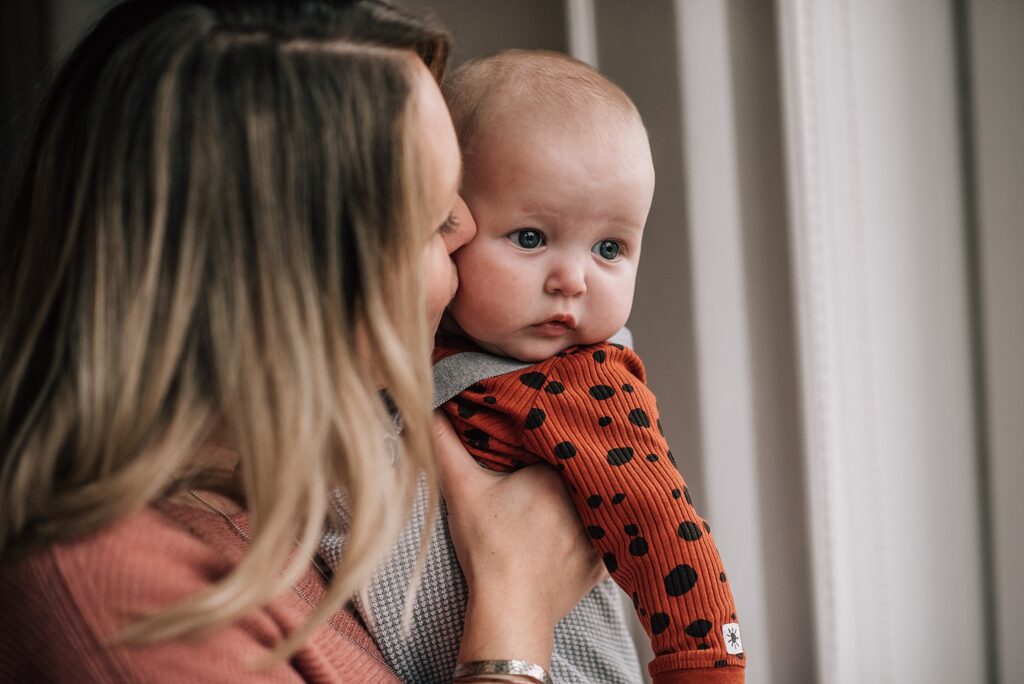 mother kissing baby next to a window frame