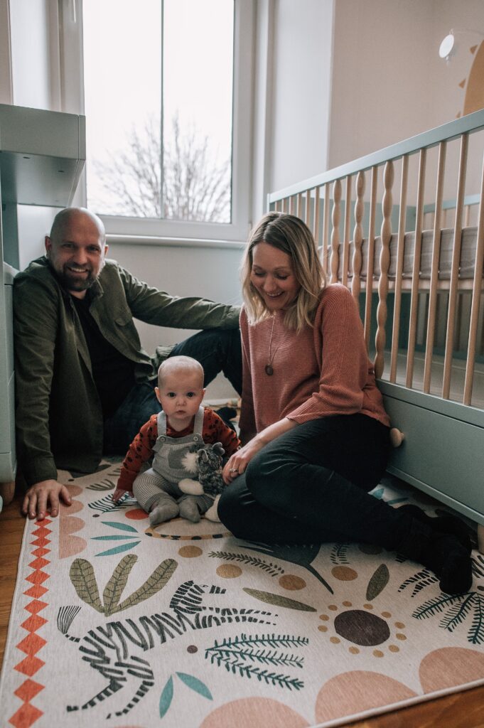 parents sitting on a rug with a baby in a nusery