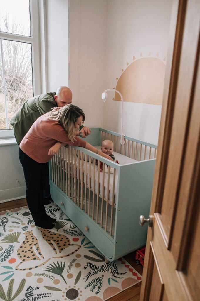 parents tending to their baby in her green crib