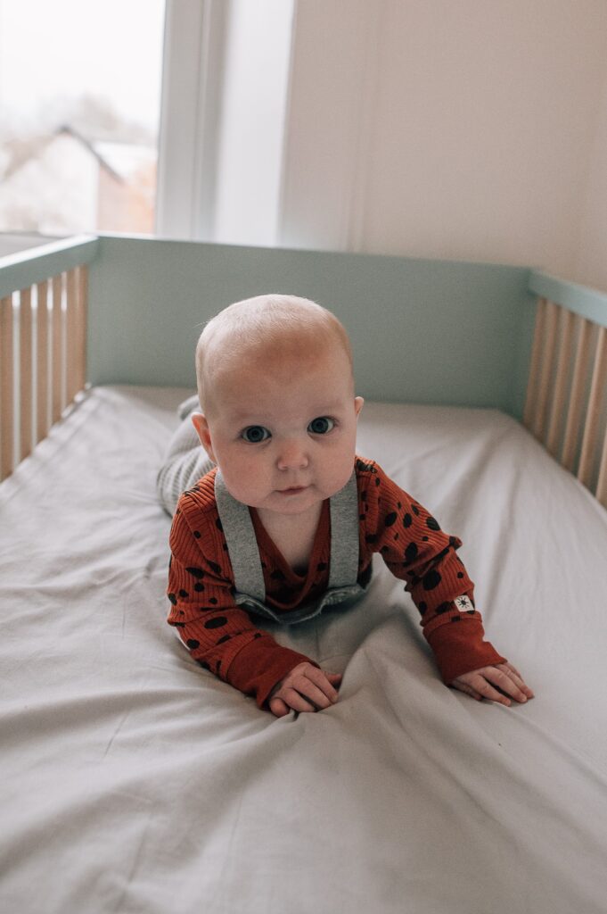 baby supporting her head and lying on tummy in a green crib
