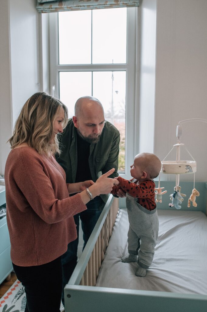 baby standing up in green crib looking at her parents