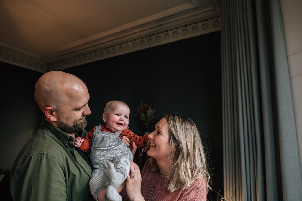baby smiling while being held by dad and smiled at by mum