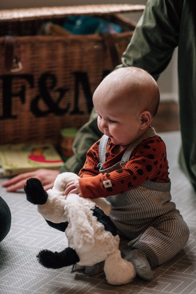 baby sitting upright and playing wit a soft toy