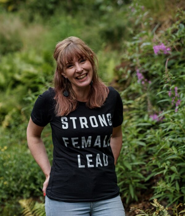 Female photographer in black tshirt that says "strong female lead" and jeans laughing and looking at the camera