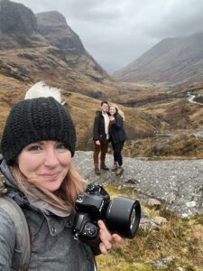 engagement photographer taking a selfie in Glencoe, Scotland with couple who recently got engaged smiling in the background
